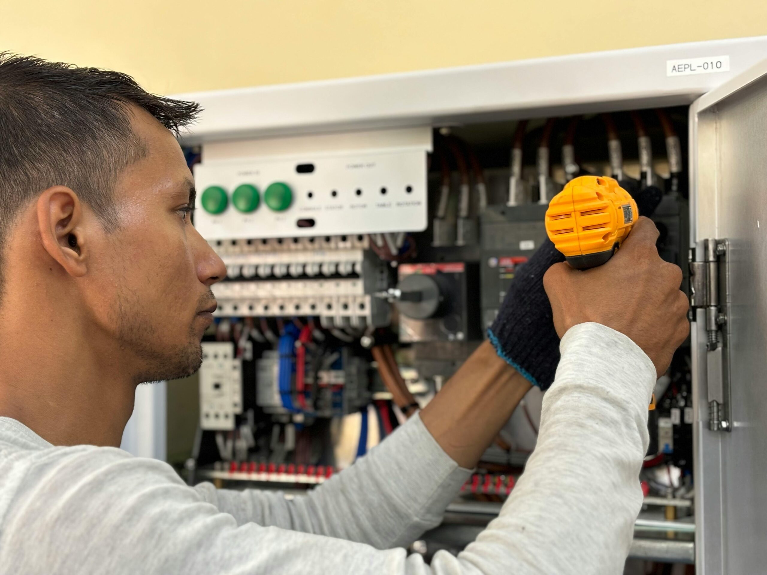 Electrician using a drill to work inside an electrical panel