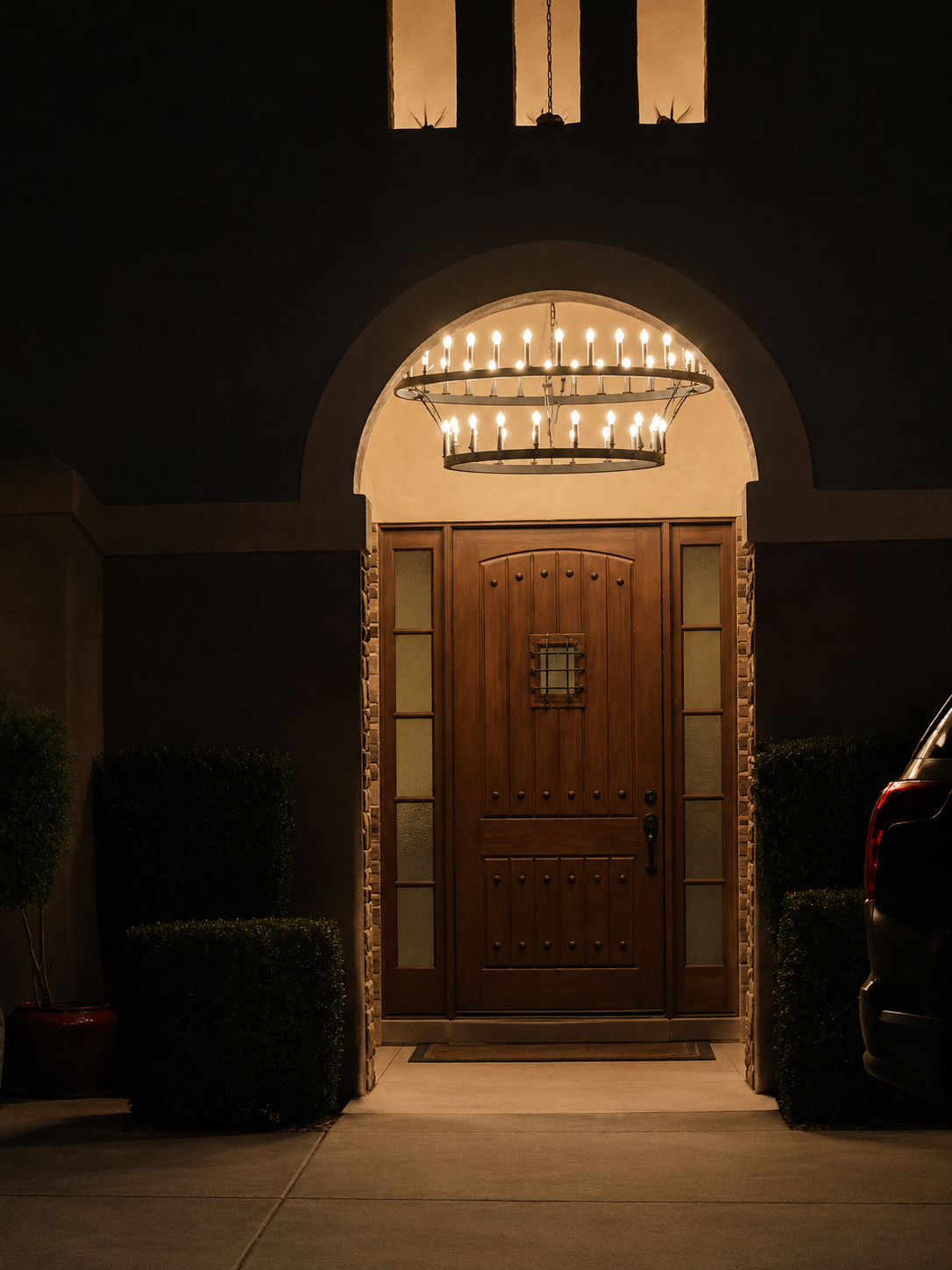 Custom home entry featuring a large circular chandelier and warm architectural exterior lighting at night.
