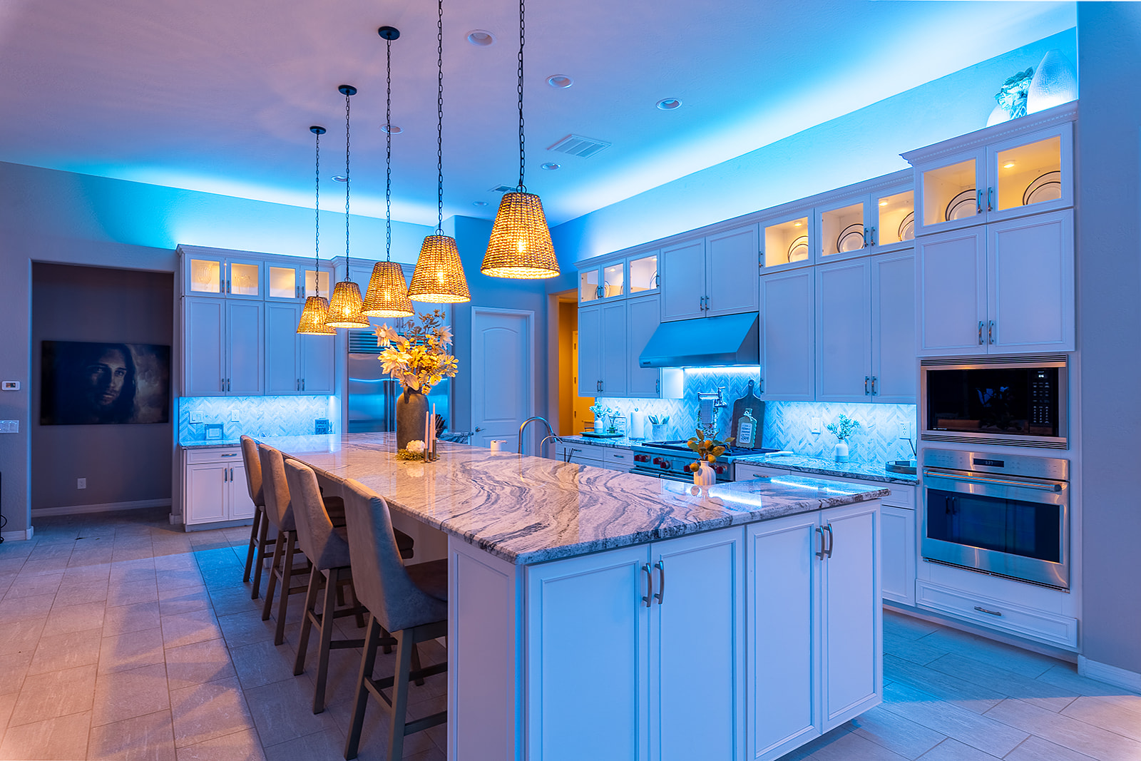 Large white kitchen with blue LED cove lighting around the ceiling, under cabinet lighting, illuminated display cabinets and pendant lights above the island.