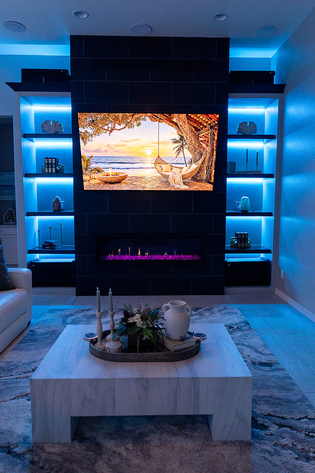Modern living room entertainment wall with blue LED illuminated floating shelves surrounding a black fireplace and mounted television.