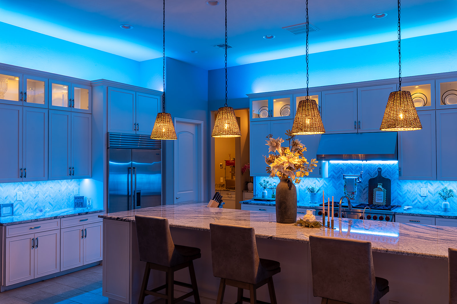Custom kitchen illuminated with vivid blue LED cove lighting and backsplash task lighting contrasted by warm pendant and cabinet lights.