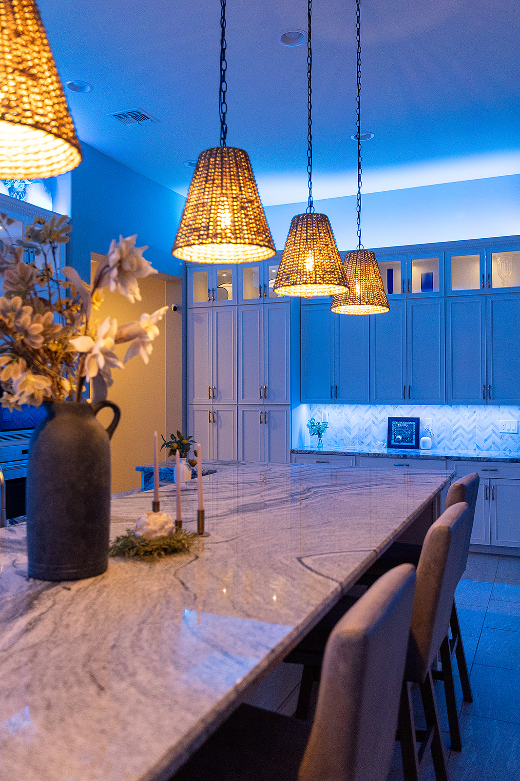 Kitchen island with warm woven pendant lights contrasted by blue LED cove lighting and bright under cabinet illumination.