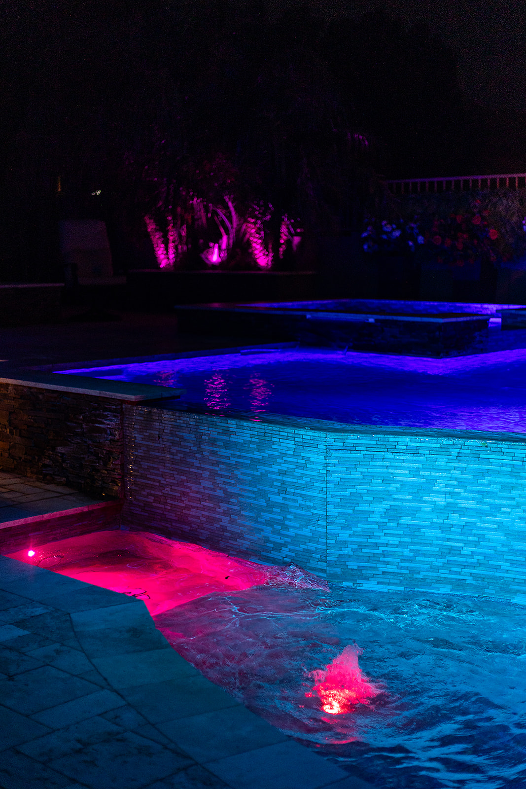 Curved pool wall illuminated blue above a lower water area with pink LED lighting and a lit bubbler.