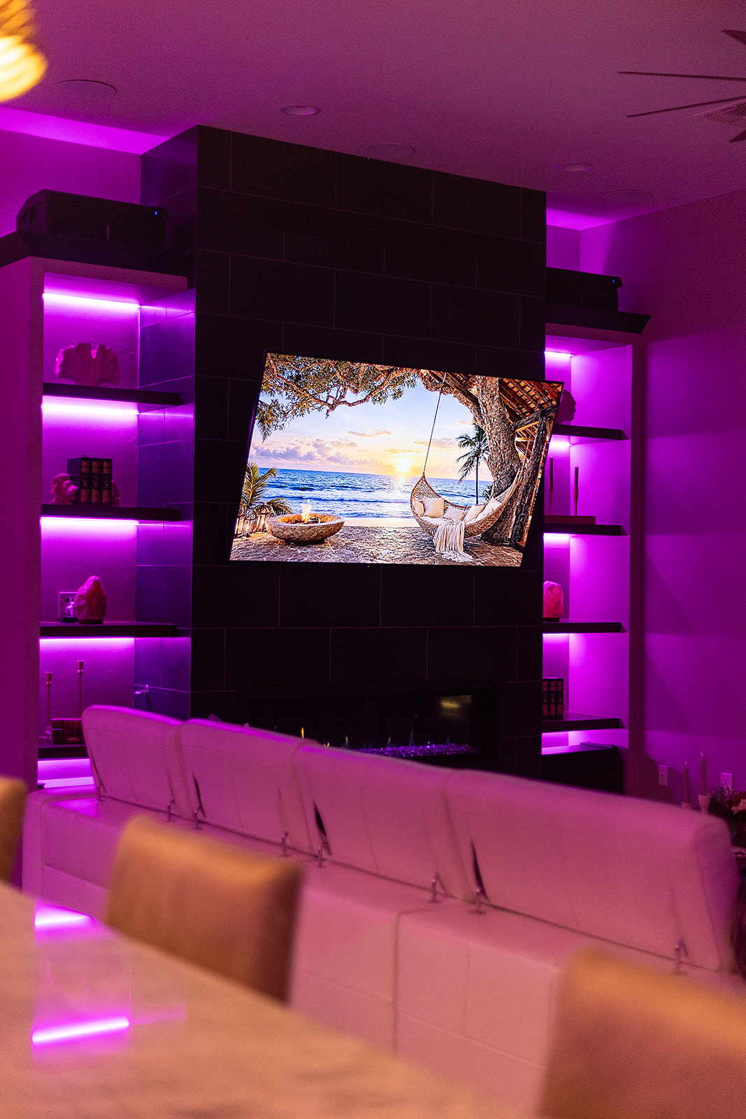 Black fireplace feature wall with a mounted television and symmetrical floating shelves illuminated by pink LED accent lighting.